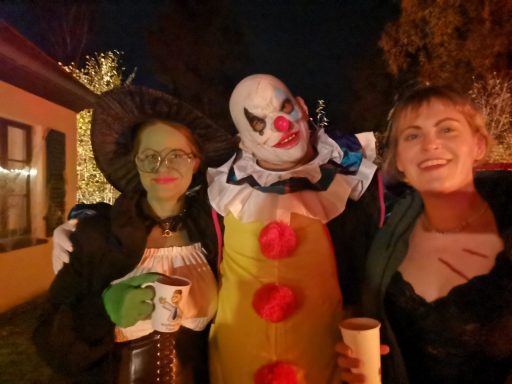 Drei Personen in Kostümen: Hexe, Clown und Lady in Schwarz, bei nächtlicher Feier.